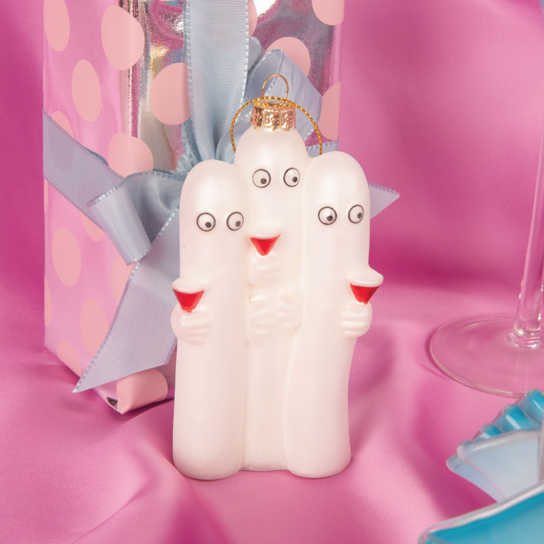 Hattifnattene julekule fra HEIM x Moomin – tre hvite håndmalte figurer i glass med røde cocktailglass, rosa bakgrunn, foran en gaveeske, del av Moomin julekolleksjonen.