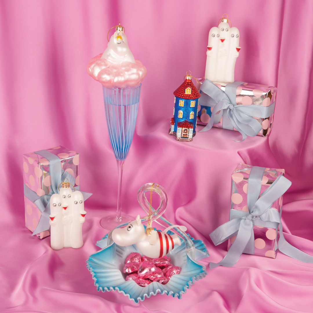 Moomin julekuler fra HEIM x Moomin – håndmalte ornamenter i glass med Mummitrollet, Mummihuset, Hattifnattene og Mummimamma på rosa bakgrunn med gaveesker.