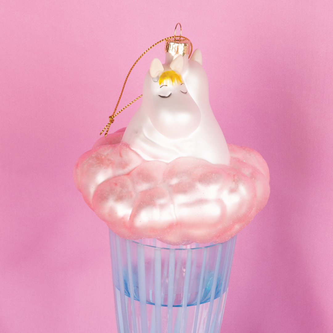 Mummitrollet og Snorkfrøken julekule fra HEIM x Moomin – håndmalt glassornament på rosa sky, romantisk og nostalgisk julepynt. Rosa bakgrunn, julekulen er plassert på et blått stettglass.