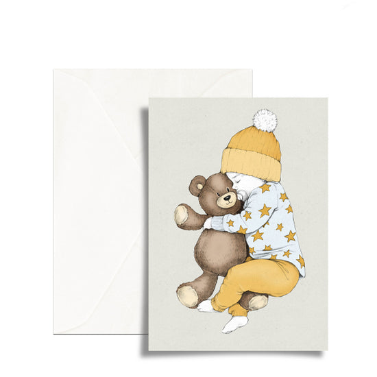 En liten baby med gule klær som klemmer en brun teddybjørn.