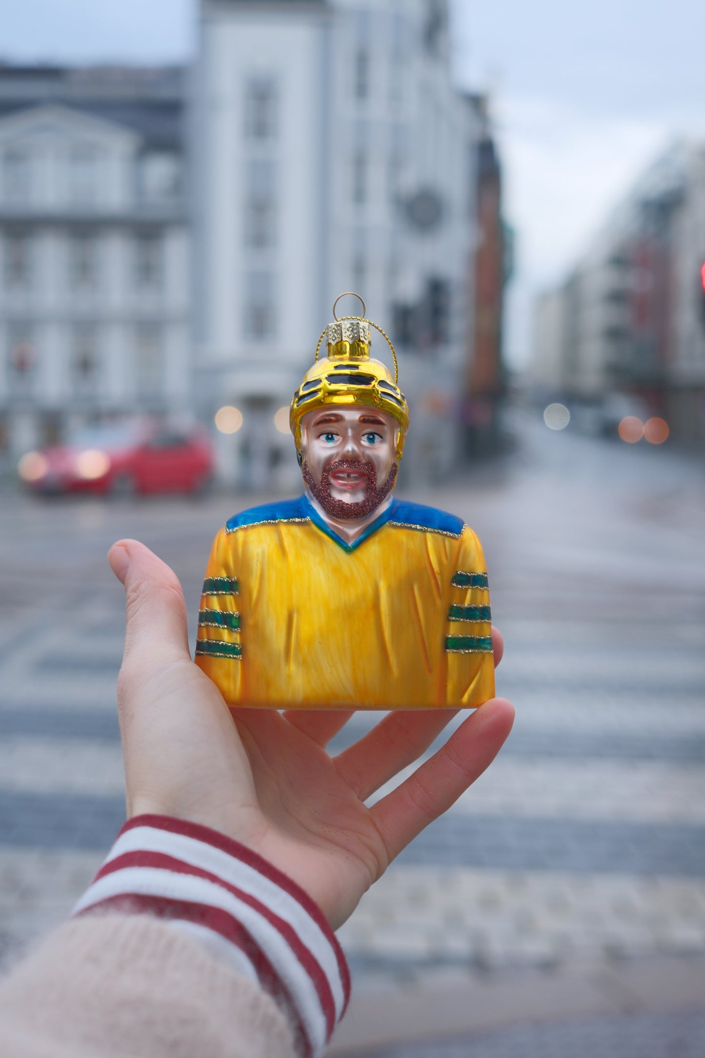Hånd som holder liten julepynt formet som ishockeyspiller med gul drakt og hjelm i urbant miljø