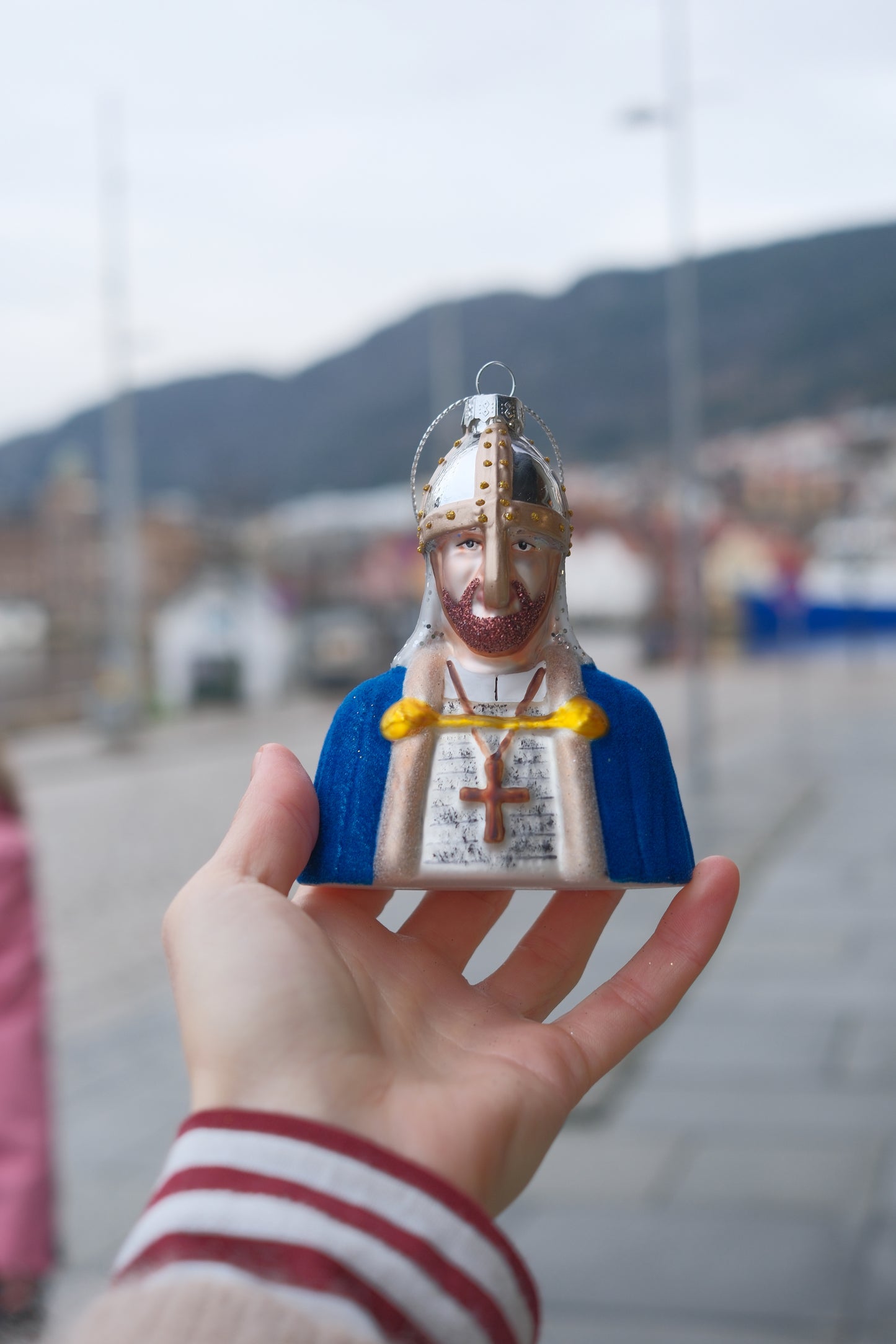 Hånd som holder dekorativ julepynt formet som middelaldermann med hjelm og blå kappe utendørs