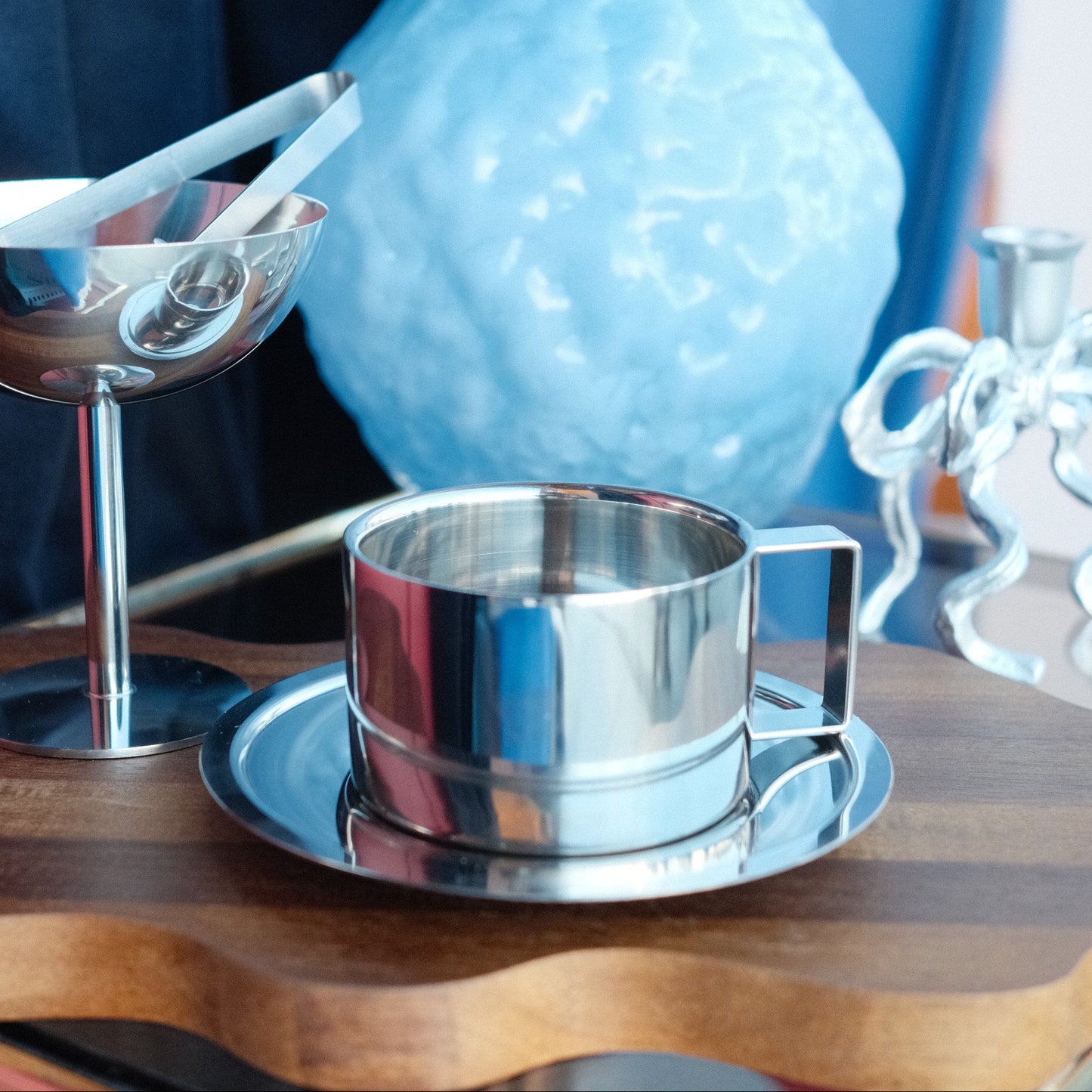 Kopp i stål - by Heim design med firkantet hank og fat i rustfritt stål på bølget treplate med skje