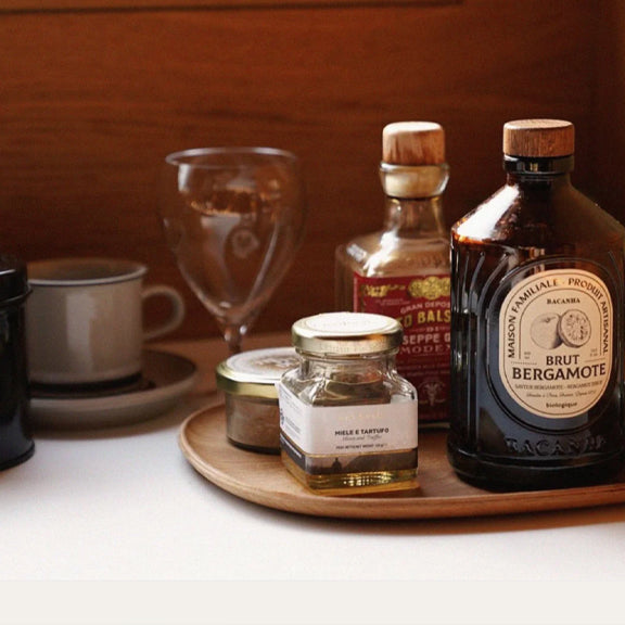 Bergamot Organic Syrup - By Bacanha i mørk flaske med trelokk på trebrett sammen med glass og krydderflaske