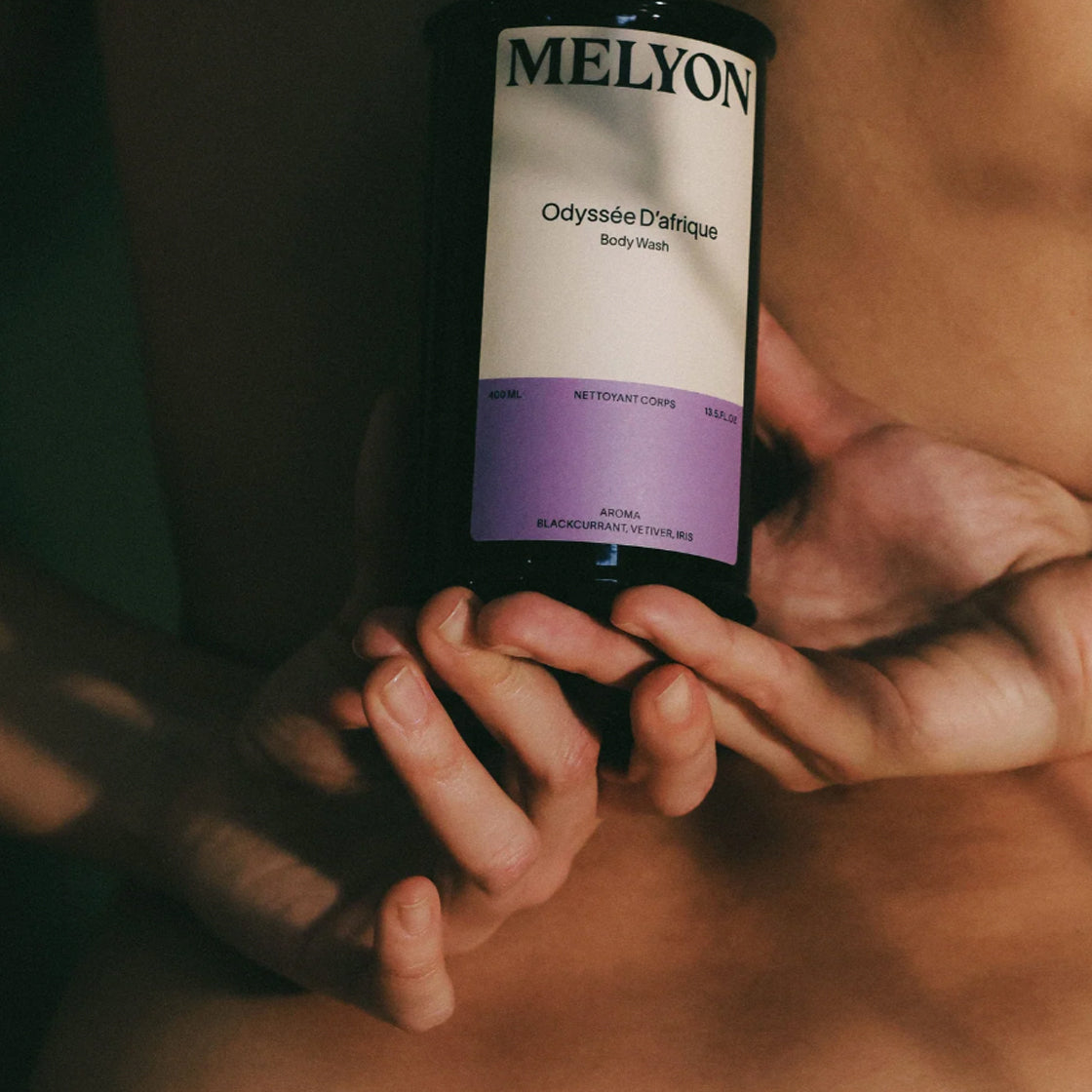 Person holder flaske med Dusjsåpe Odyssée D´afrique  - By Melyon i varmt, dempet lys