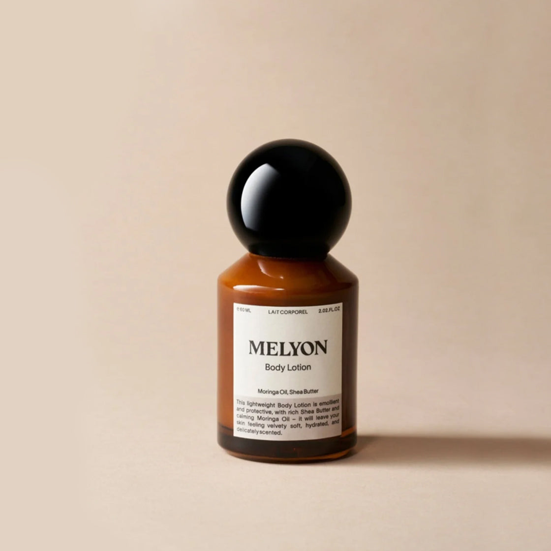 Brun flaske med rund svart kork for Body Lotion Shea Butter 60 ML - By Melyon på varm beige bakgrunn