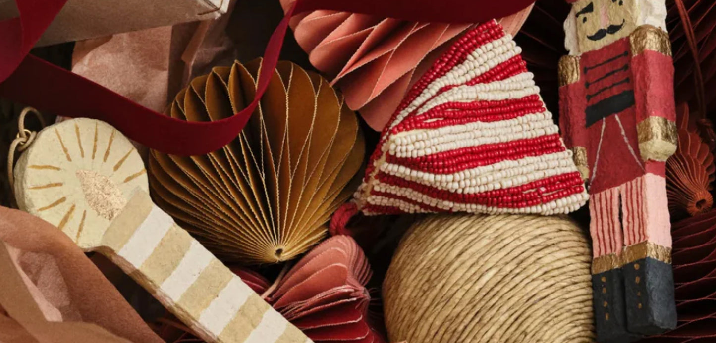 Håndlaget nissehatt, trefigur og papirpynt i varme røde og beige toner i juledekorasjonstilbehør