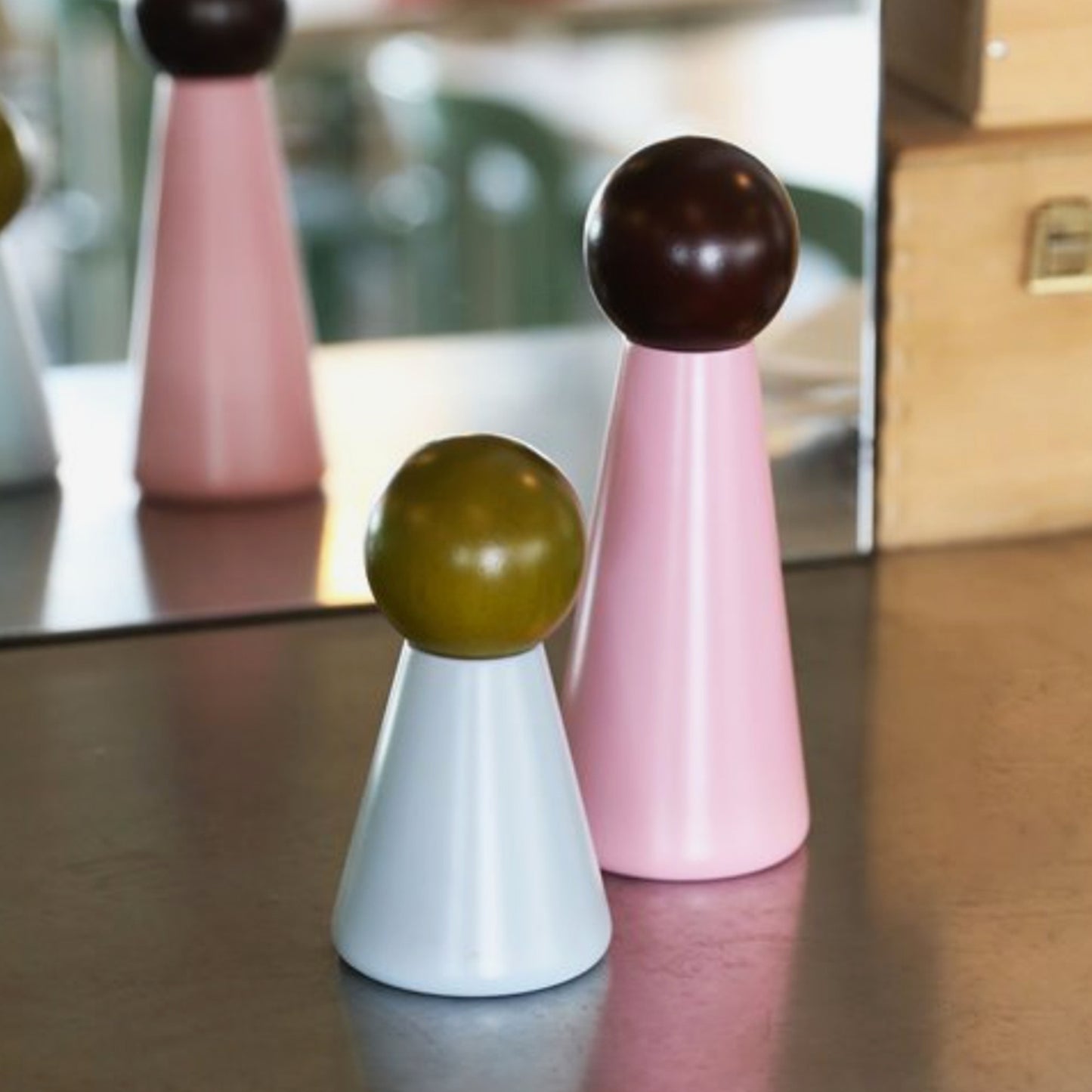 To kjegleformede bordsalt- og pepperbøsser i rosa og hvitt med runde topper plassert på bordflate foran speil