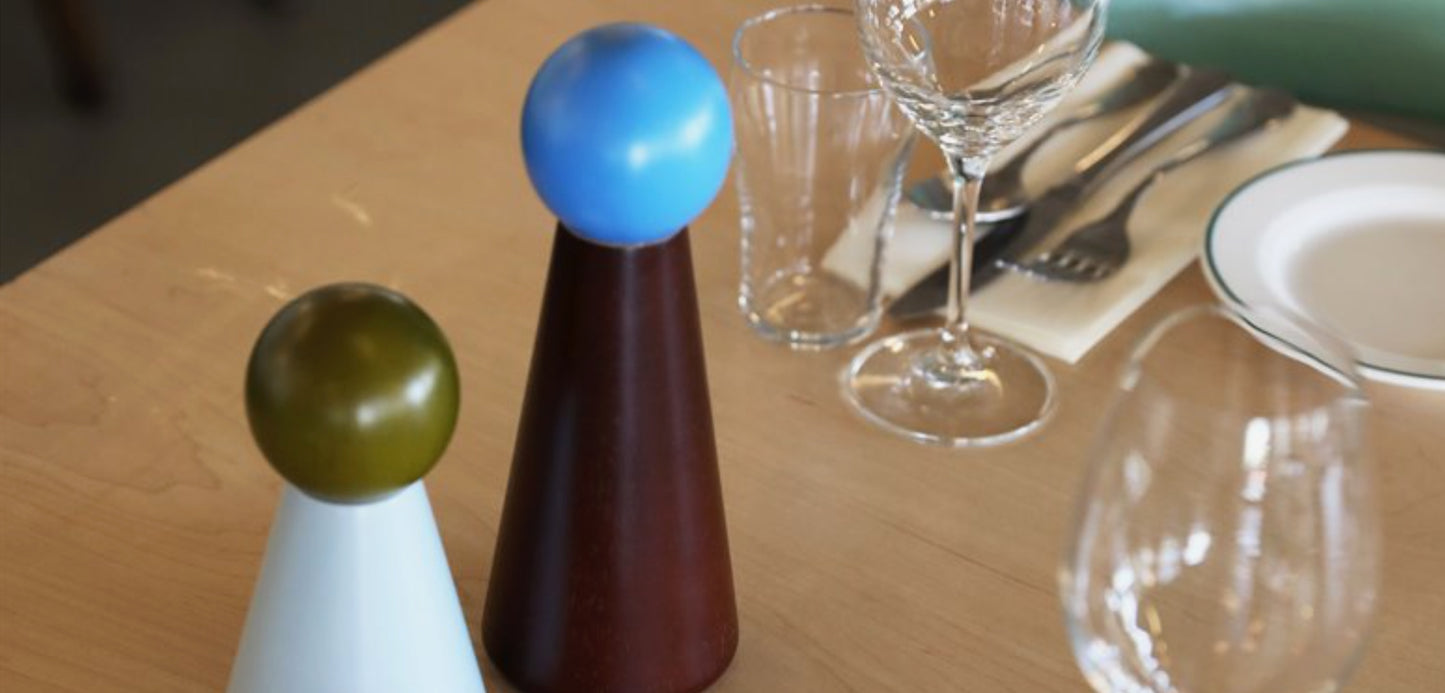 To kjegleformede bordsalt- og pepperbøsser med fargede kuler på toppen plassert ved dekket bord
