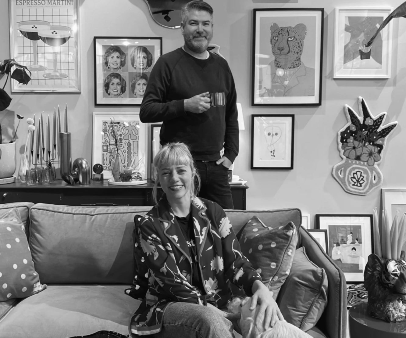 To smilende personer i stue med kunstverk og dekorative puter på sofa i bakgrunn med bilder på vegg