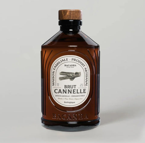 Brunt glassflaske med treskrukork og hvit etikett med kanelstangillustrasjon mot grå bakgrunn