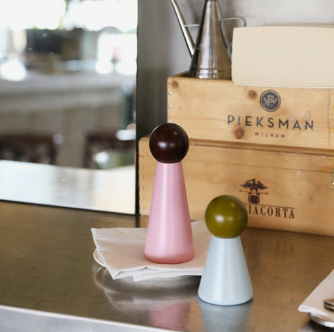 To kjegleformede salt- og pepperbøsser i rosa og lyseblå med runde topper plassert på bord ved serviett