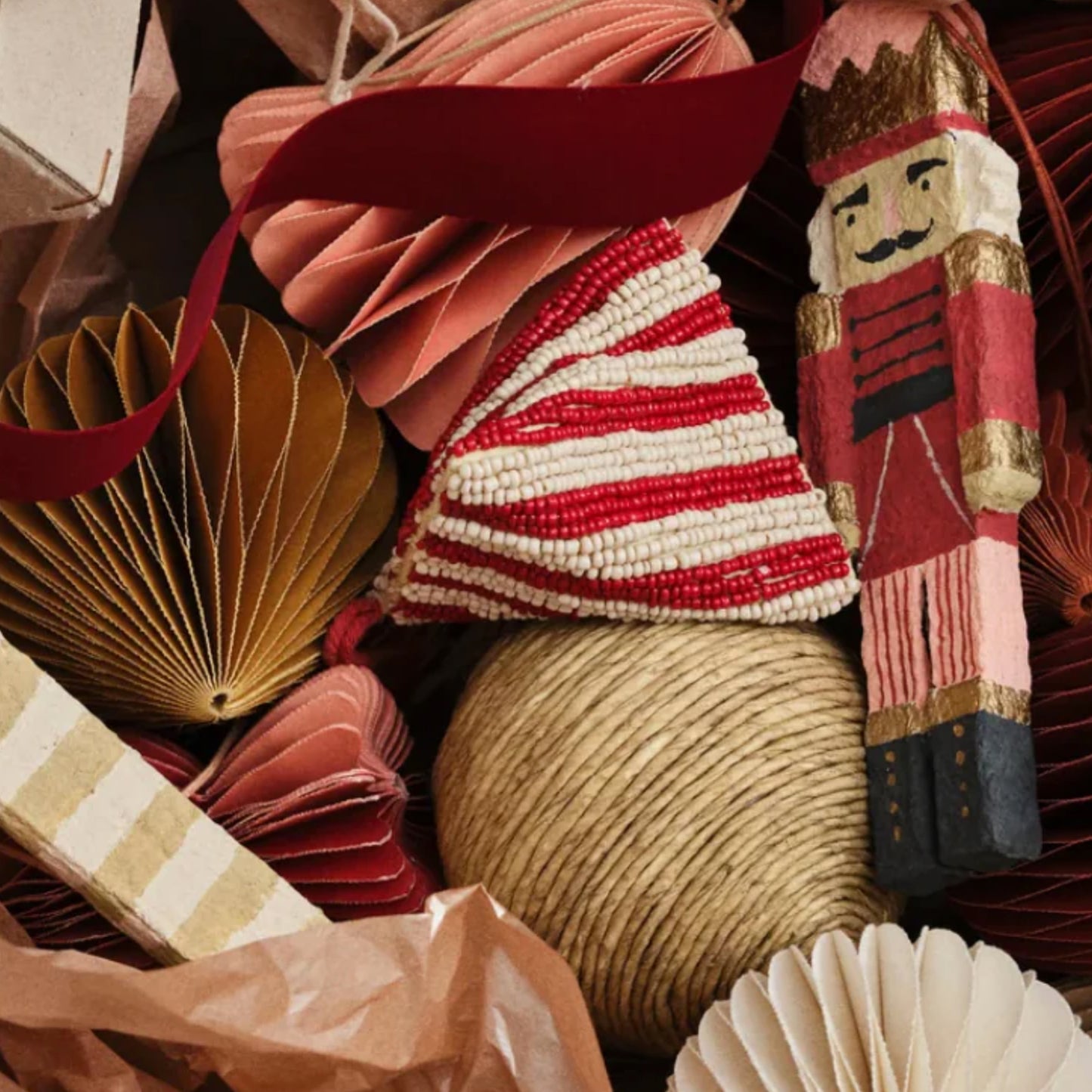 Papirpynt i varme jordfarger sammen med kule av twine, perlebrodert julepynt og en tresoldat med rød drakt