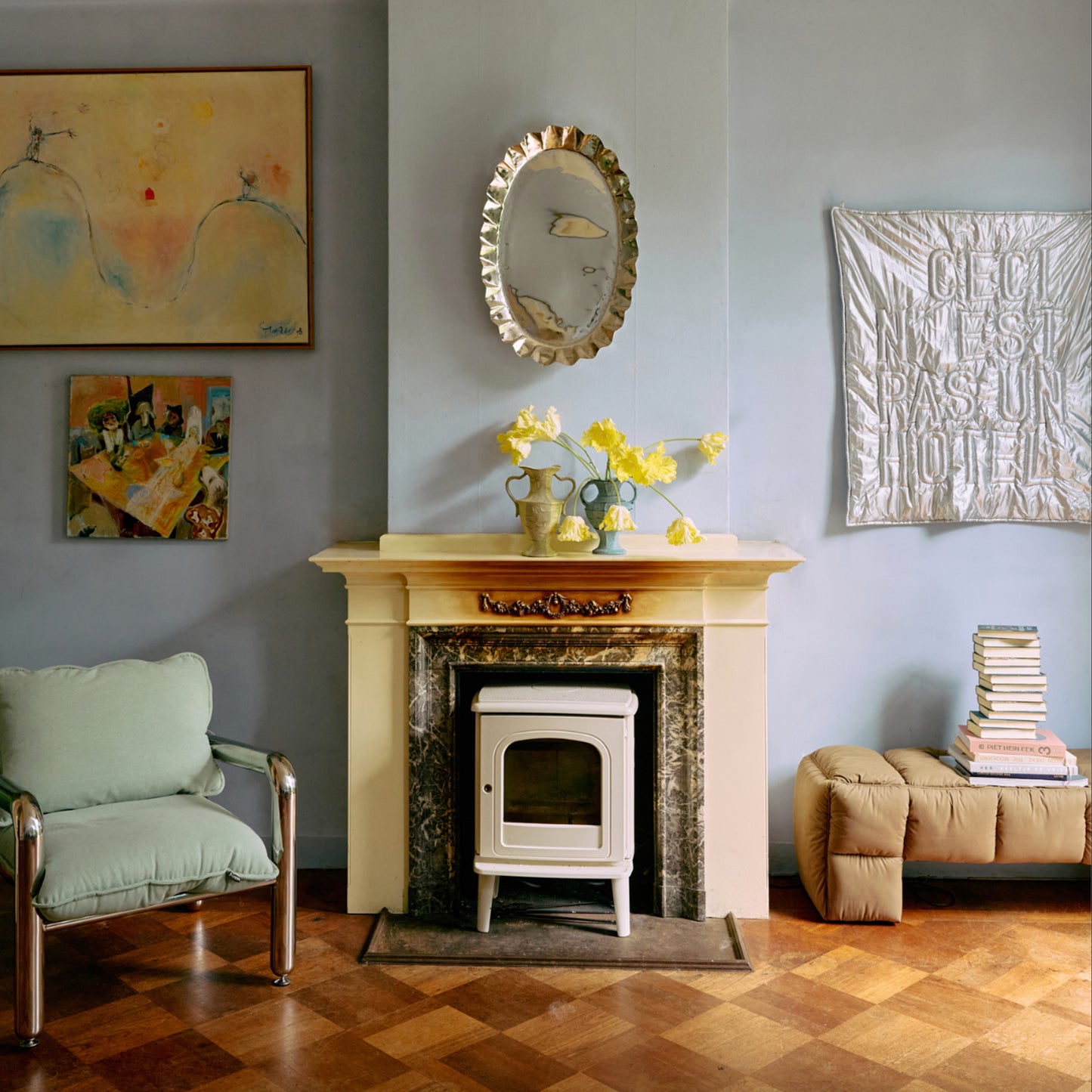 Stue med liten hvit ovn i dekorativ peis, speil med bølget ramme og gule blomster i vaser på åpningen